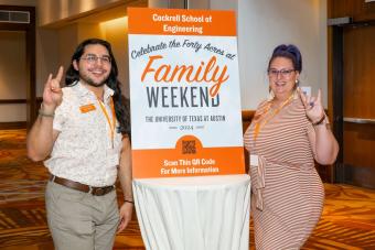 Two people showing “hook-em” hand sign standing at Cockrell School of Engineering table