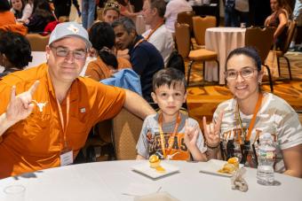 Three people sitting at table showing “hook-em” hand signs