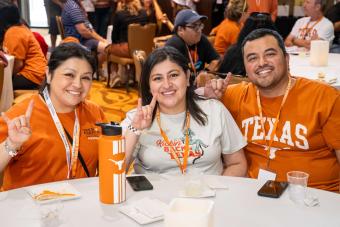 Three people sitting and showing “hook-em” hand signs