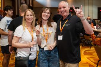 Three people smiling, two are showing “hook-em” hand signs