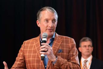 UT Austin President Jay Hartzell on stage holding mic with a person in the background