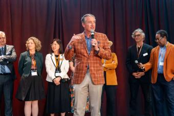 UT Austin President Jay Hartzell on stage holding mic with seven people standing behind