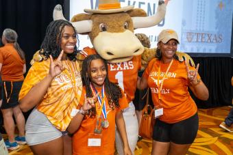 Hook ‘Em mascot posing with three people and showing Hook ‘Em hand signs