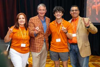 UT Austin President Jay Hartzell posing with three people and showing Hook ‘Em hand signs