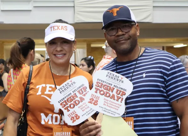 Couple holding Texas Parents' Sign Up Today hand fans at UT's Family Orientation