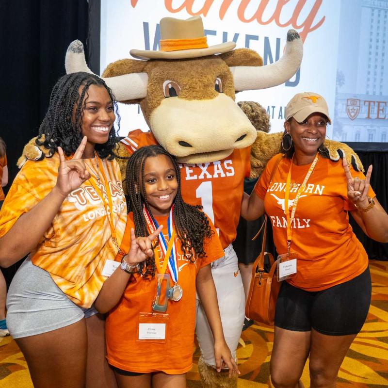 UT Austin’s Hookem mascot with three family members flashing hook em horns hand sign at Family Weekend Reception