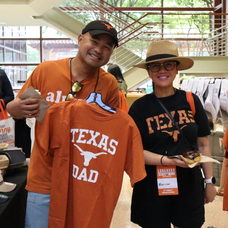 Couple holding Texas Dad shirt inside Gregory Gym at UT's Family Orientation