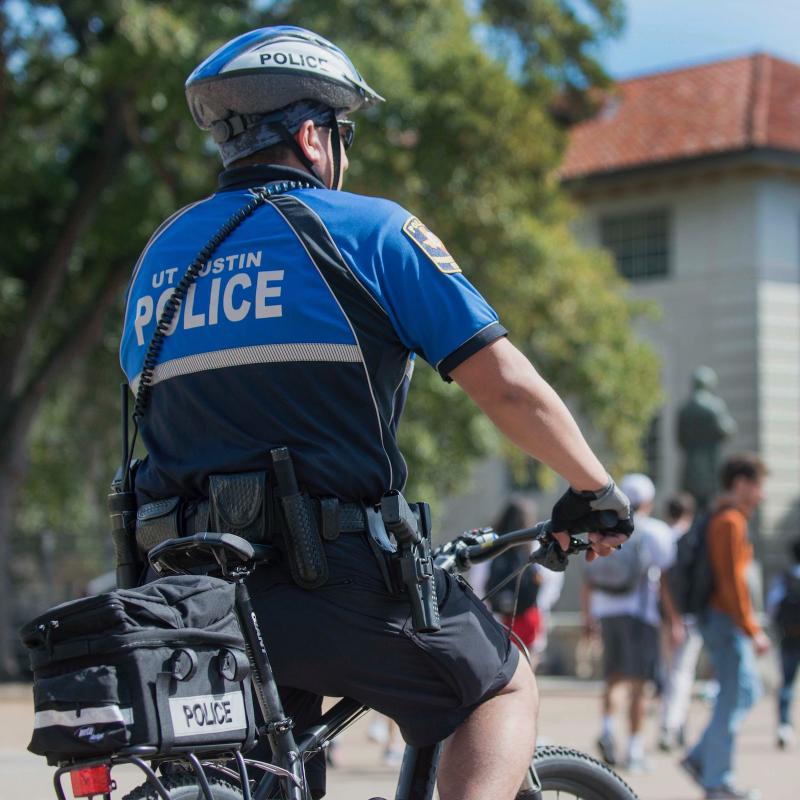 UTPD officer on bicycle on UT Austin's main mall photographed from behind